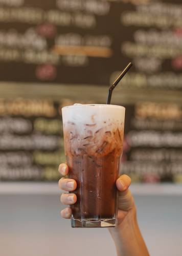A hand holding up a cold brew latte. This appears on the top of the how to make a cold brew latte page of Bean Merchant's website.