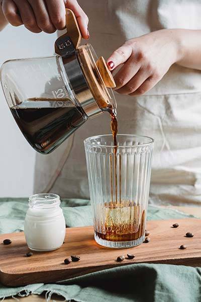 Pouring cold brew coffee into a homemade iced coffee glass, on the top of Bean Merchant's How to make homemade Iced Coffee Page
