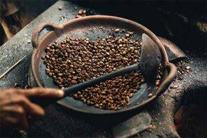 A man roasting coffee beans in an iron skillet. The different variety of coffee beans impact flavour, this blog on Bean Merchant's website talks about how.